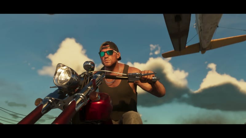 A muscular man in a backwards cap and green sunglasses rides a red motorbike as a small plane passes low overhead against a blue, cloudy sky.