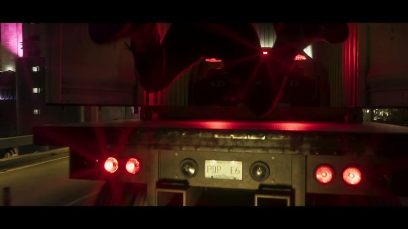 The back of a lorry trailer at night, with glowing red tail lights and a Liberty City number plate reading PDP E6, on a road beside lit buildings.