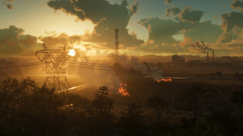 Aerial view of Leonard County as fires burn in farmland at sunset in Ambrosia, with a pylon, a mast and factory chimneys against a cloudy orange sky.
