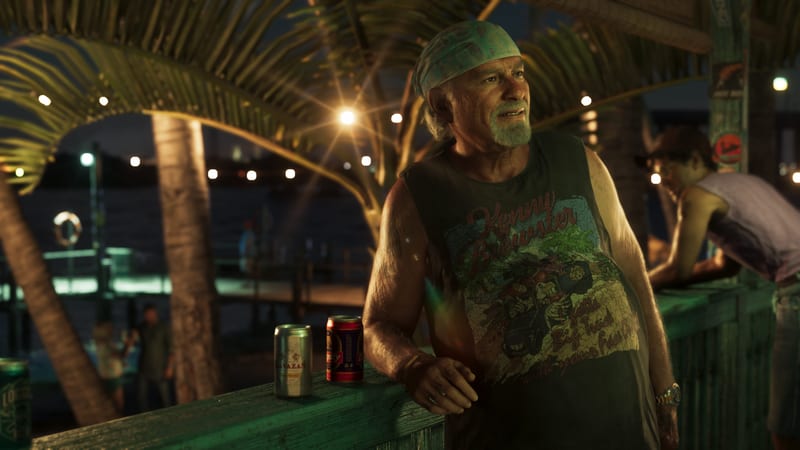 Brian Heder, an older man in a green bandana and sleeveless T-shirt, leans on a wooden railing beside two beer cans at a waterside bar at night.