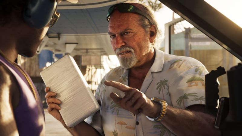 Brian Heder, an older man in a palm-print shirt, points while a person in the foreground holds a wrapped white brick, in bright sunlight.