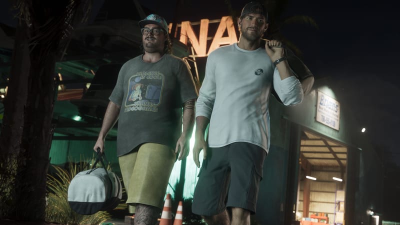 Two men in caps and shorts walk at night carrying holdalls past a boatyard building with a lit sign, one in a graphic T-shirt and one in a white top.