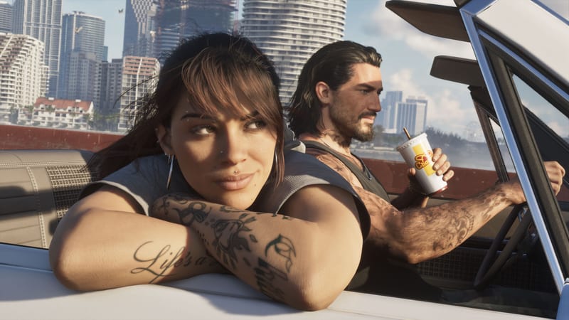 Lucia Caminos rests her tattooed arms on a car door while Jason Duval drives beside her, a city skyline of tall towers behind them.