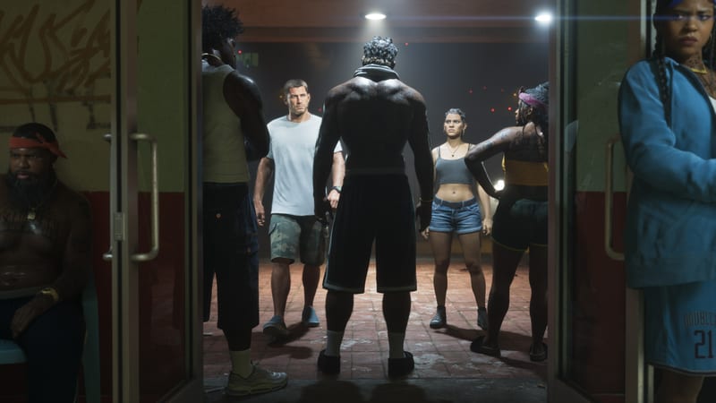 Jason Duval and Lucia Caminos stand among a group of tough-looking people around a shirtless man seen from behind, in a doorway at night.