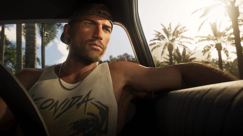 Jason Duval sits in the driver's seat of a car, arm resting on the seat back, looking out past palm trees in strong sunlight.