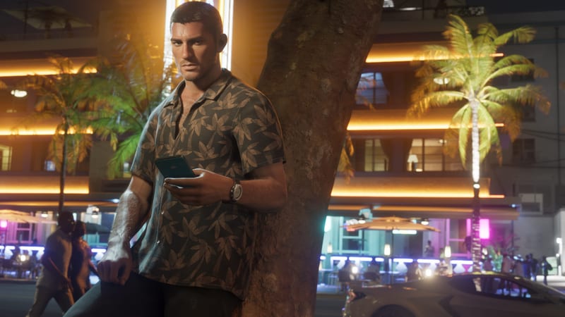 Jason Duval leans against a palm tree trunk holding a phone, on a street at night with neon-lit hotels behind him.