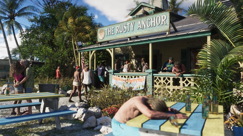 A shirtless man slumped asleep on a picnic table outside The Rusty Anchor bar, with a crowd and a couple embracing on a sunny day in Leonida Keys.