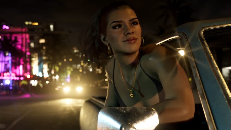 Lucia Caminos leans out of a battered blue pickup window at night, smiling, with neon-lit buildings and car headlights blurred behind her.