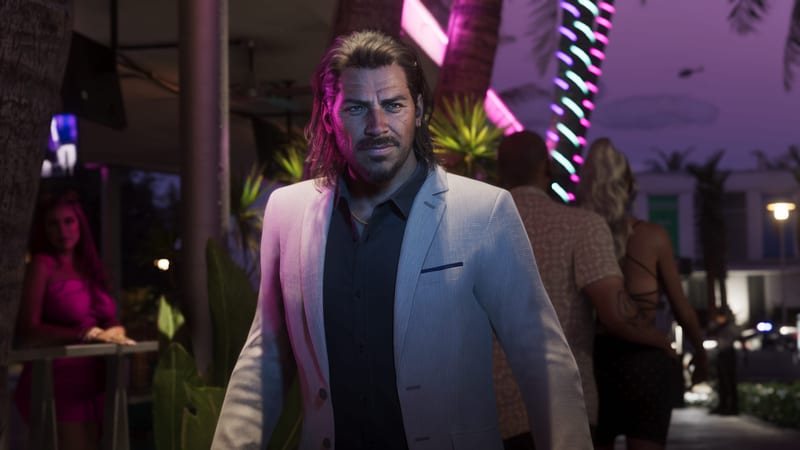 Raul Bautista, a long-haired man with a moustache and goatee in a white jacket, stands on a neon-lit palm-lined street at night.