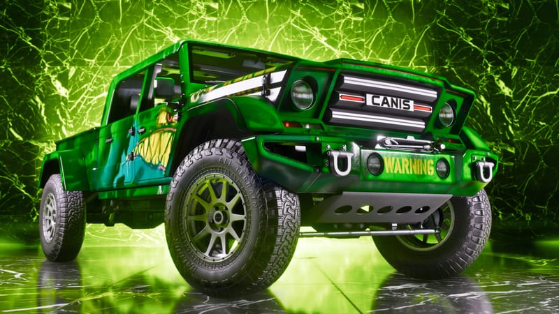 A green Canis four-door pickup truck with a monster mouth design and WARNING on the bumper, parked on a shiny floor before a glowing green marble wall.