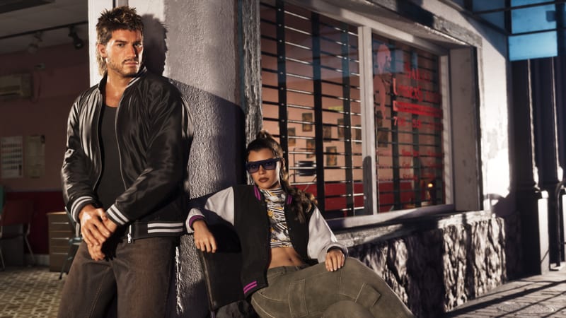 A man in a black bomber jacket stands against a wall beside a seated woman in sunglasses, outside Sara's Unisex Salon, in strong sunlight.