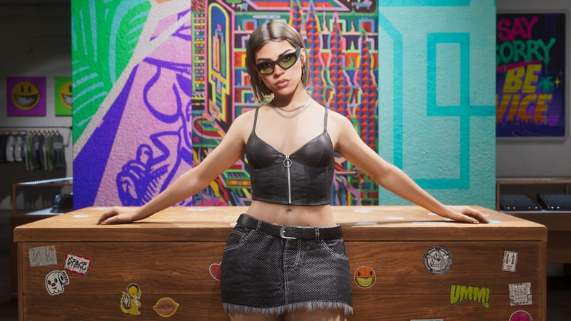 Lucia Caminos stands with arms outstretched on a wooden shop counter covered in stickers, in front of colourful murals, wearing green-lensed sunglasses.