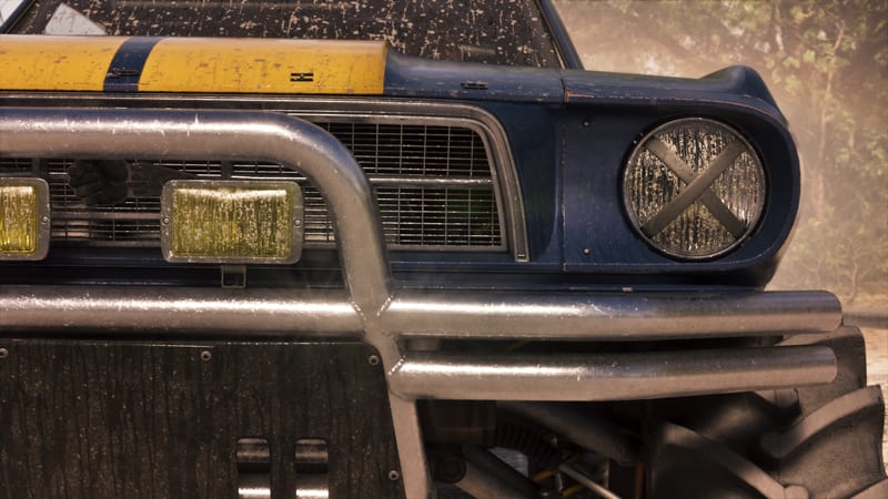 Close-up of the mud-splattered front of a blue and yellow lifted '67 Vapid Dominator Buggy with a steel bull bar, in a hazy wooded setting.