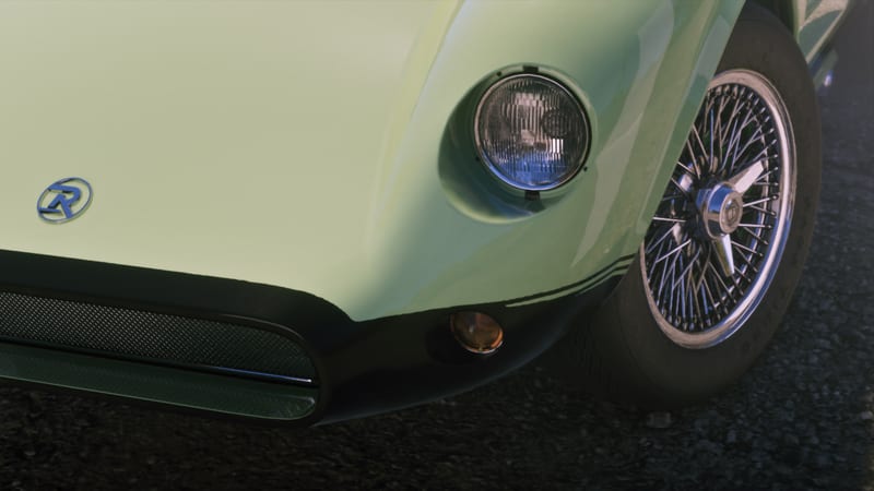 Close-up of the front corner of a pale green classic sports car with a round headlight, wire-spoke wheel and a blue R badge on the bonnet.