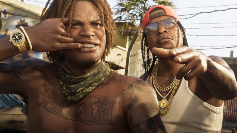 Two men pose close to the camera on a sunlit street, one shirtless with a green bandana and gold grills, the other in a red cap and sunglasses.